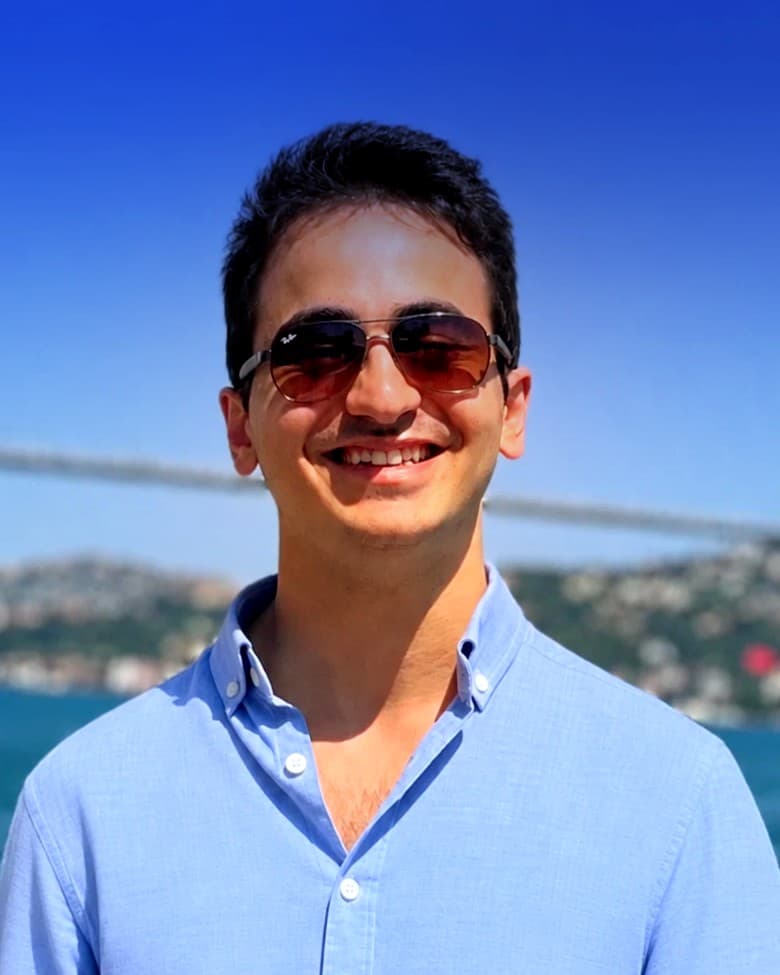 Ömer Faruk Ballı, smiling, in a light blue shirt by the water